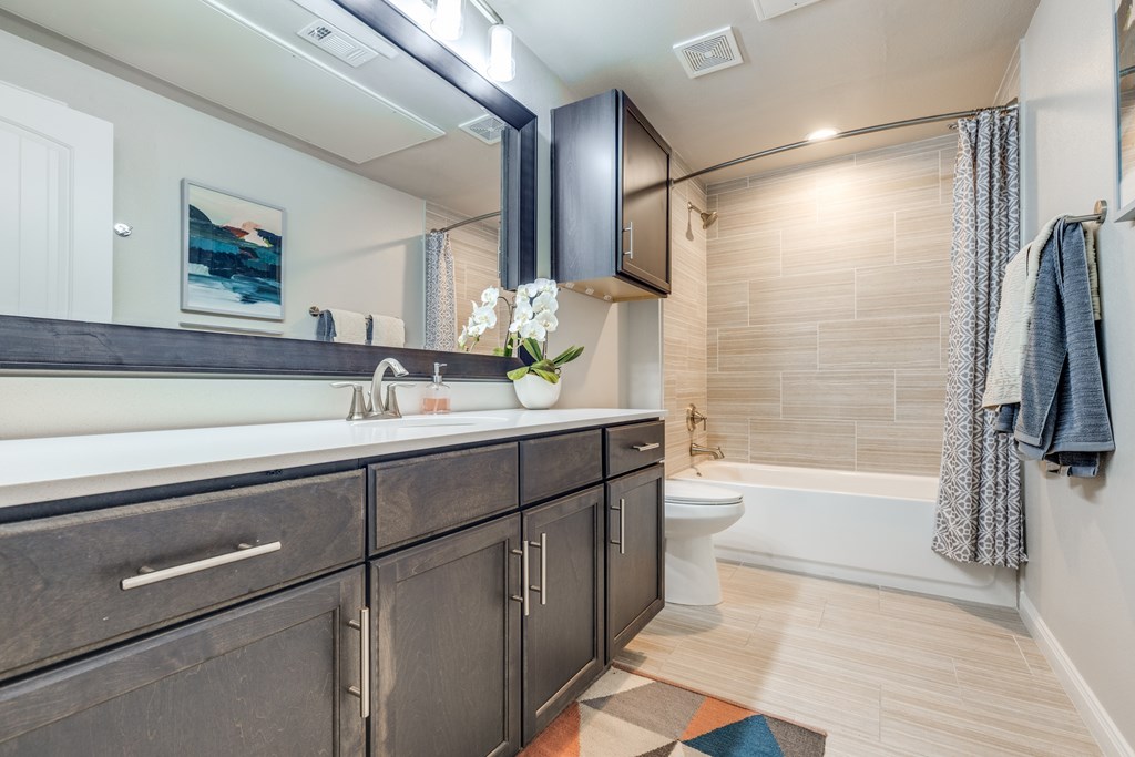A bathroom with a white toilet, a sink with a mirror above it, and a bathtub with a shower curtain.