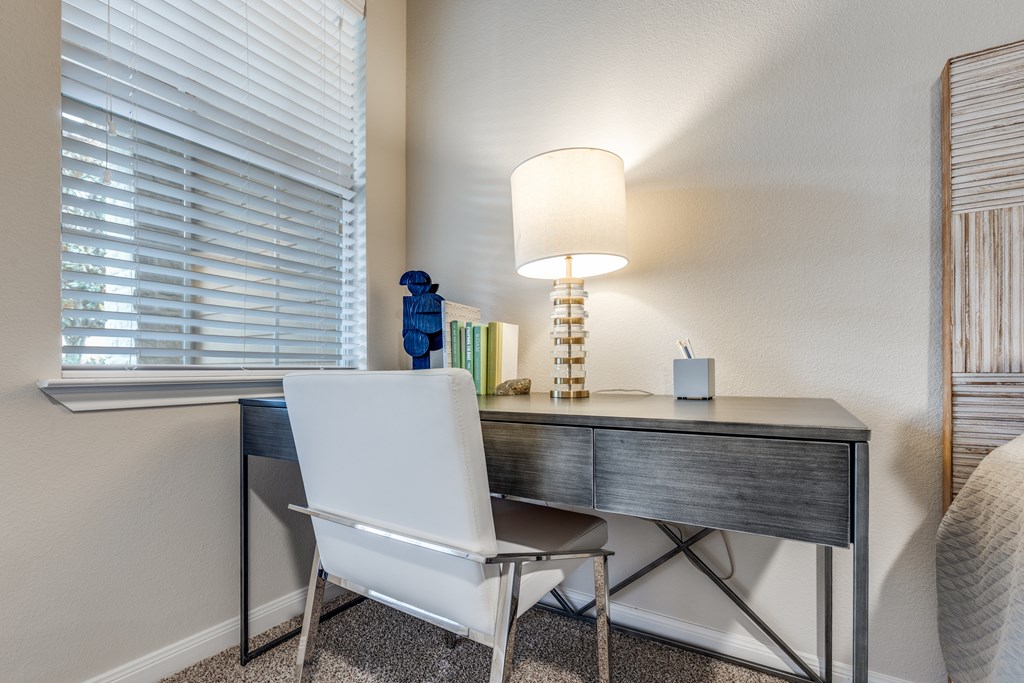 A white chair sits in front of a desk with a lamp on it.