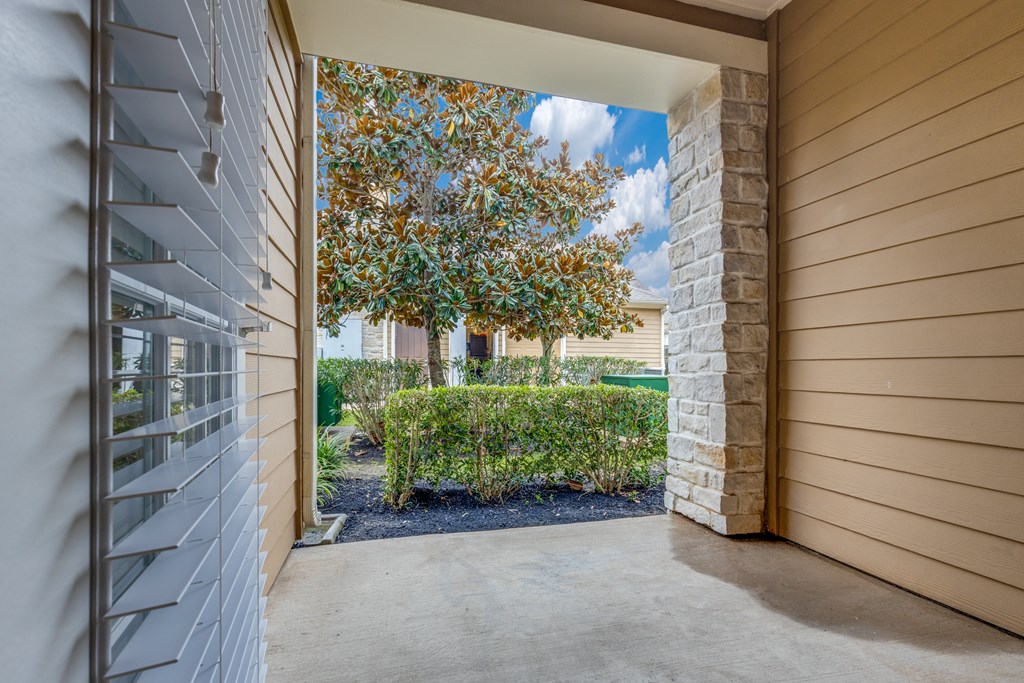 A view from a covered walkway looking out to a tree and shrubs.