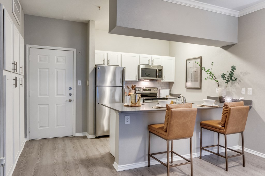 an open kitchen with stainless steel appliances and a counter with two chairs