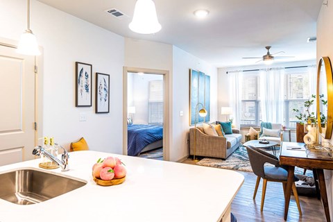 A kitchen with a white countertop and a sink with a bowl of fruit on it.