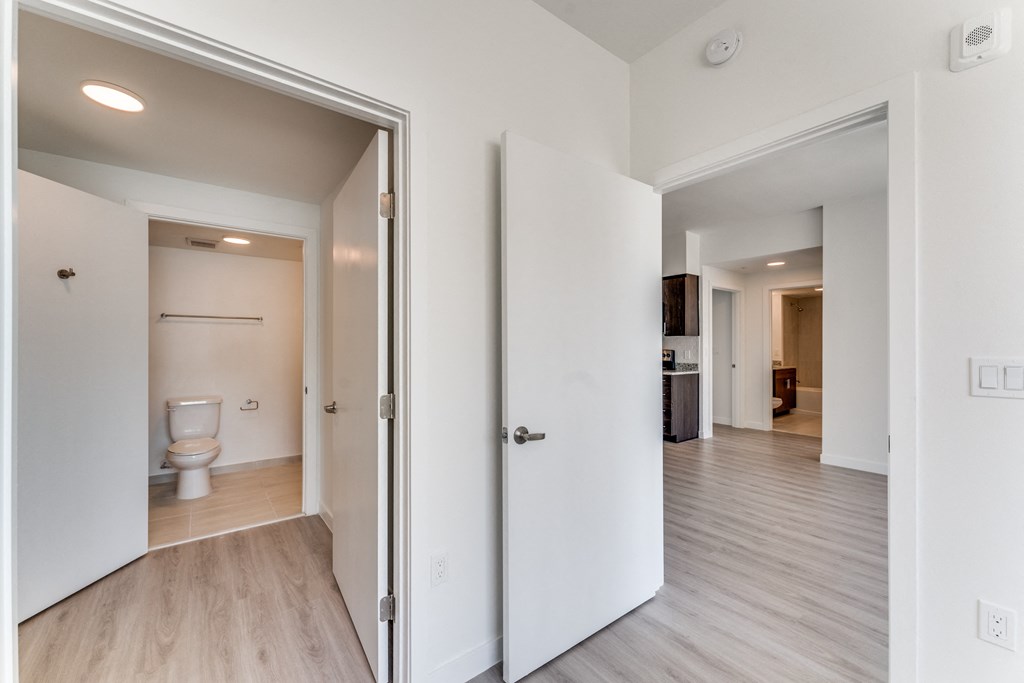 a bedroom with a door to a bathroom and a hallway with a toilet