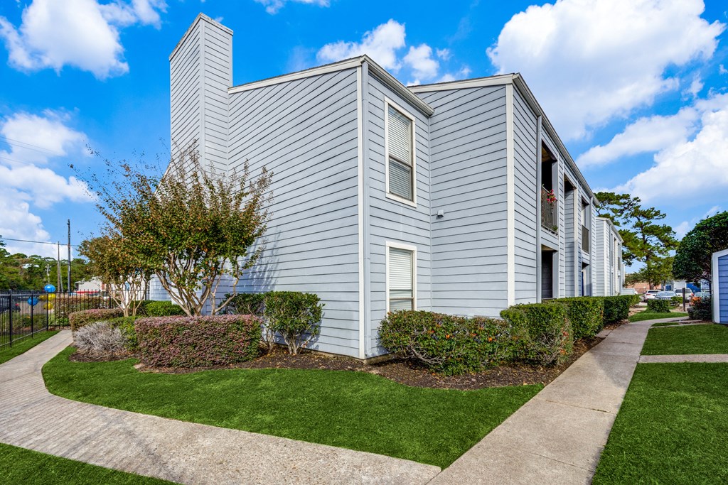 an apartment building with blue siding and a sidewalk and green grass