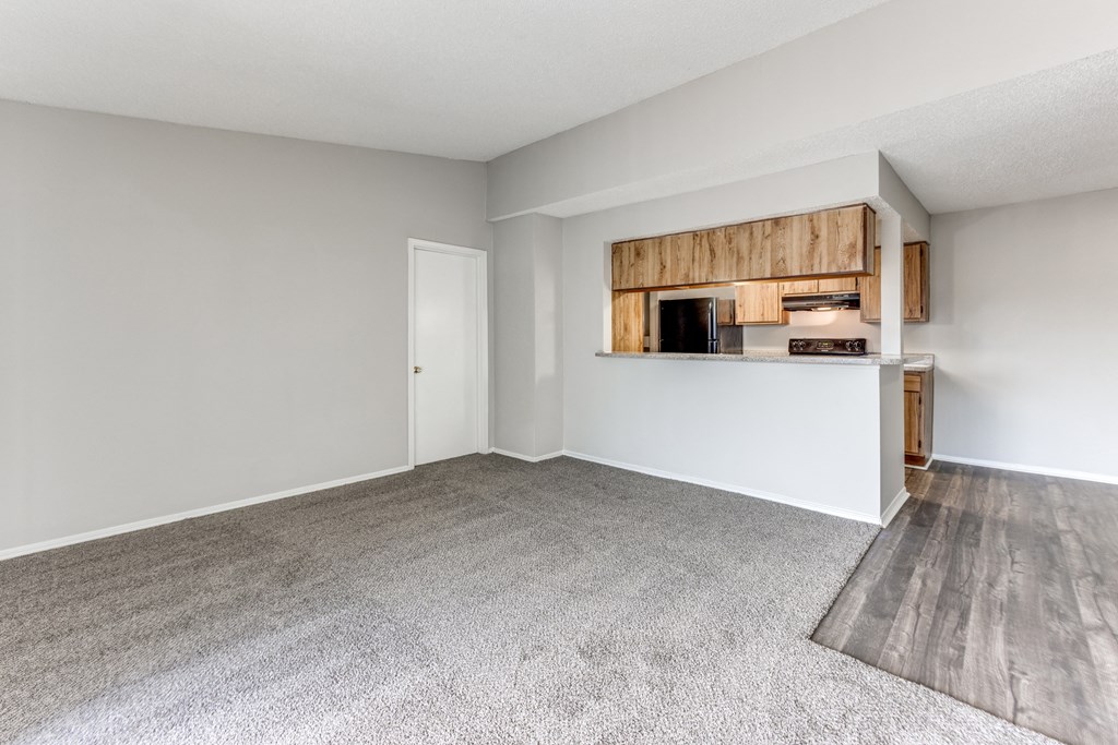 an empty living room with a kitchen in the corner