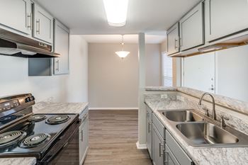 A kitchen with a stove, sink, and cabinets.