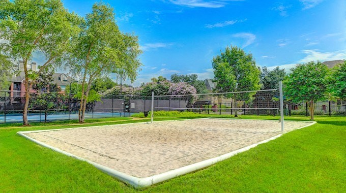 A sand volleyball court surrounded by a fence and trees.