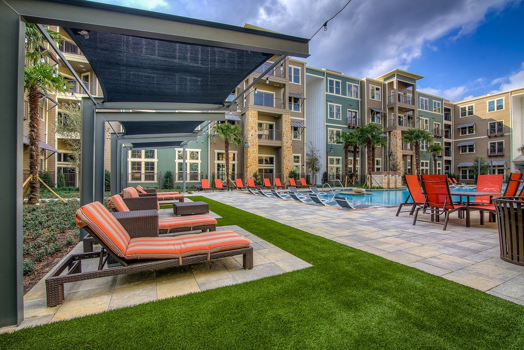 a patio with lounge chairs and a pool in front of an apartment building