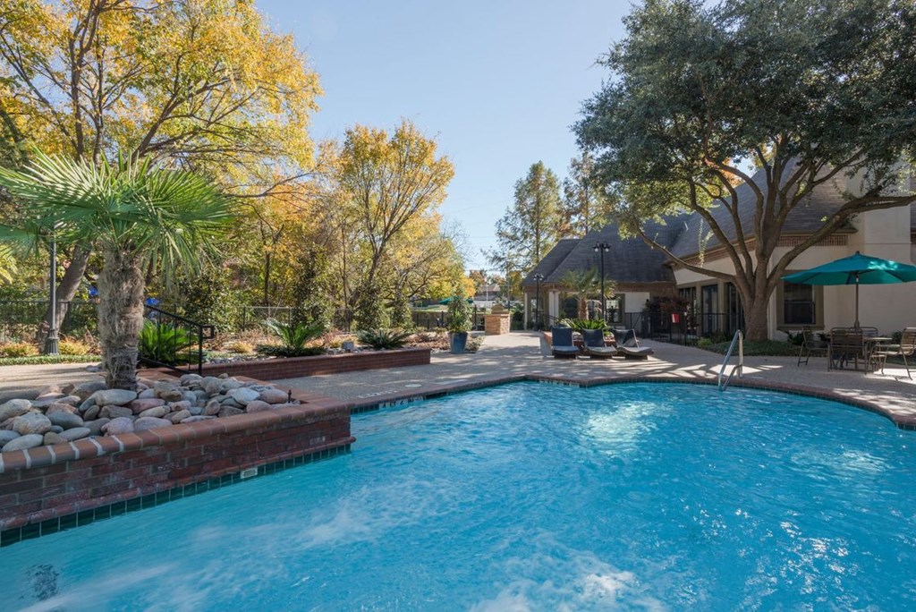 a swimming pool with blue water and a patio with chairs and umbrellas
