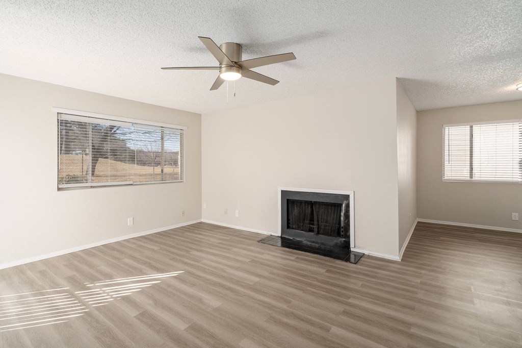 an empty living room with a fireplace and a ceiling fan