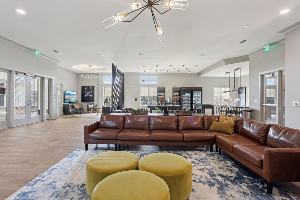 A large brown leather couch is in the middle of a spacious room with a chandelier hanging from the ceiling.