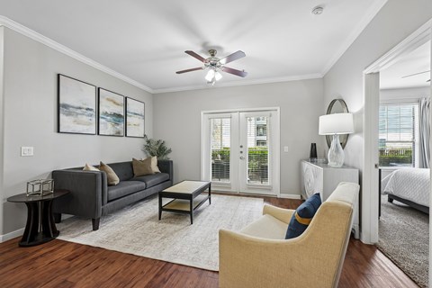 A living room with a grey couch, a beige armchair, a coffee table, and a ceiling fan.