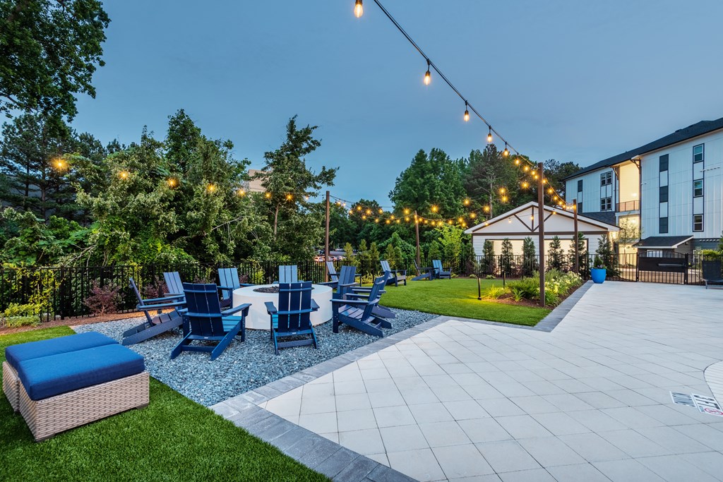a patio with blue chairs and a table and a seating area with lights hanging above