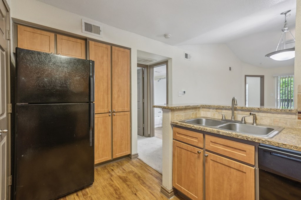 A black refrigerator sits in a kitchen with wooden cabinets and a granite countertop.