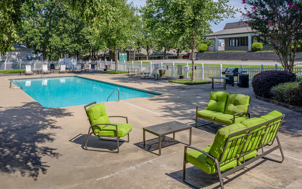 a swimming pool with green chairs and tables around it
