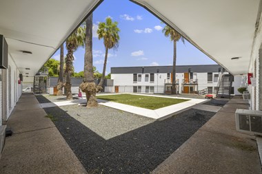 a courtyard with a grassy area and palm trees in front of a white building
