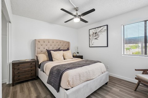 A bedroom with a large bed, a ceiling fan, and a window with blinds.