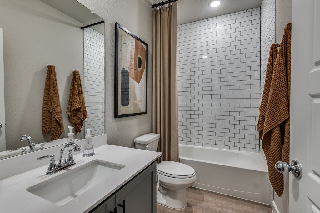 A bathroom with a white sink, toilet, and a shower with a brown towel hanging on the door.
