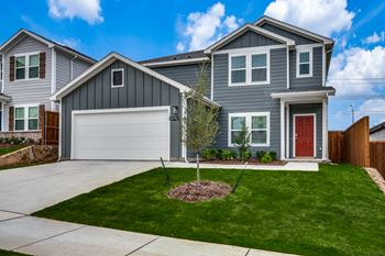 A grey house with a red door and a small tree in the front yard.