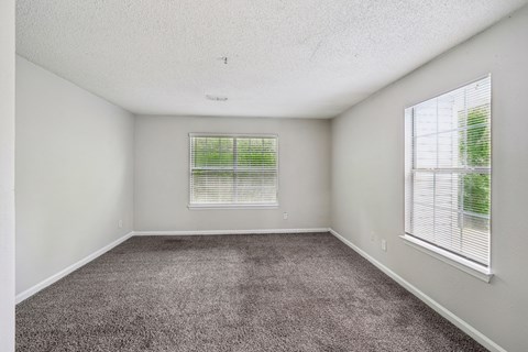A room with a carpeted floor and two windows with blinds.
