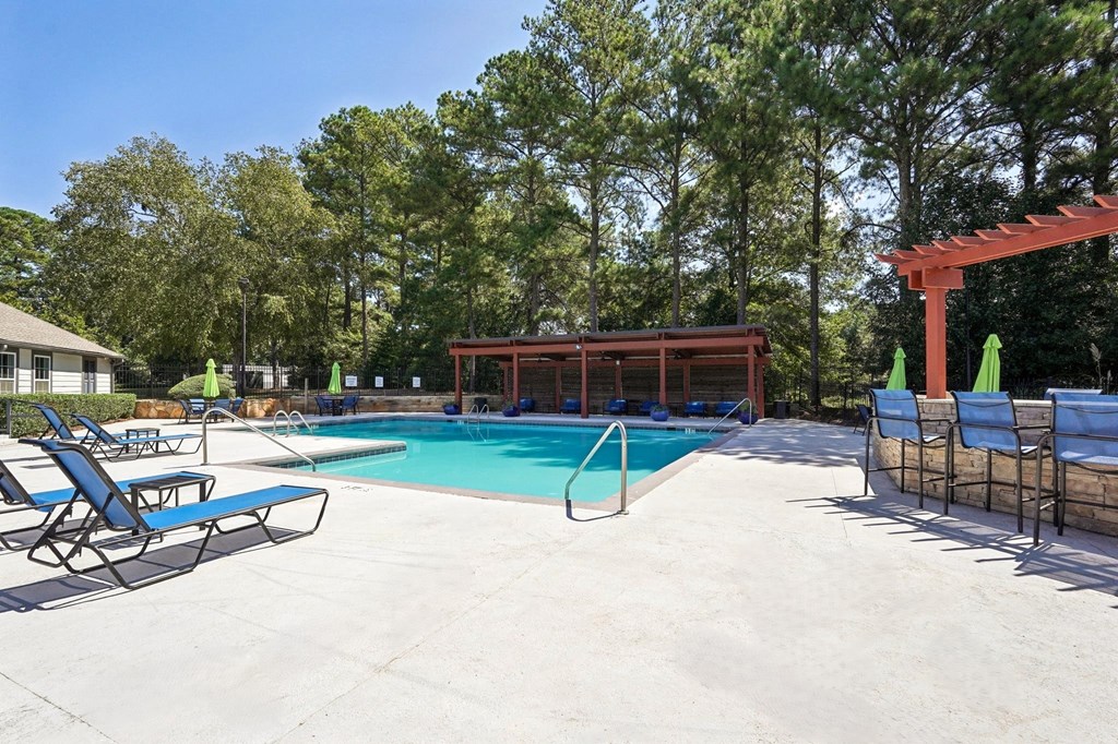 A pool area with a red pergola and lounge chairs.