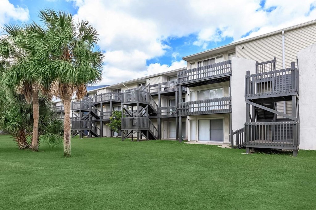 the backyard of an apartment building with green grass and palm trees