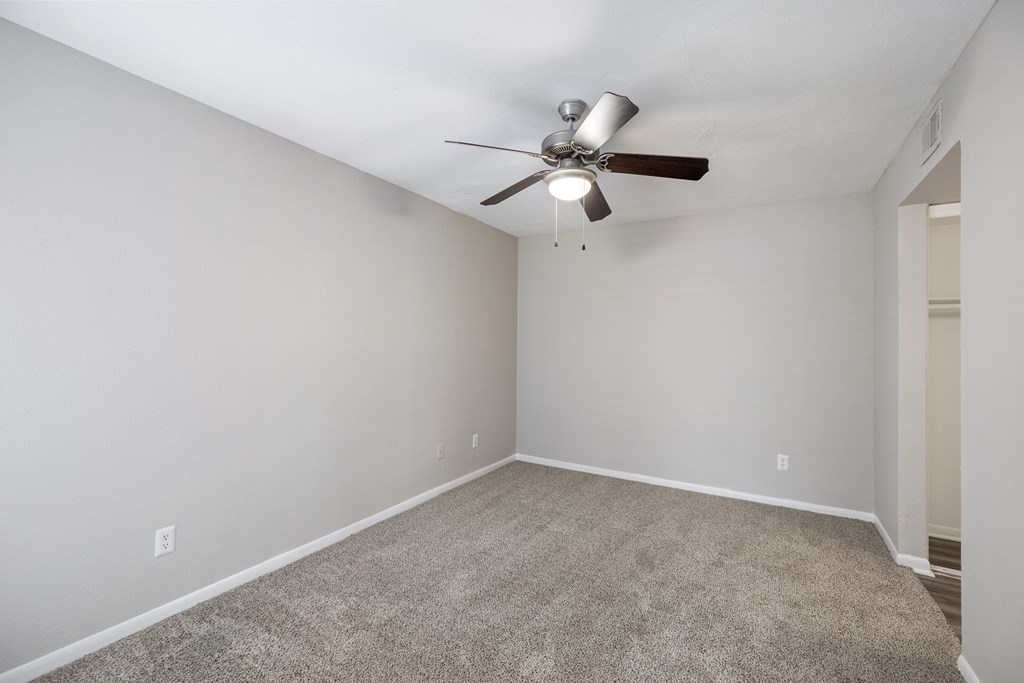 an empty room with a ceiling fan and a carpet