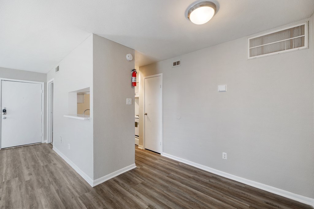 the living room and dining room of an apartment with white walls and wood flooring