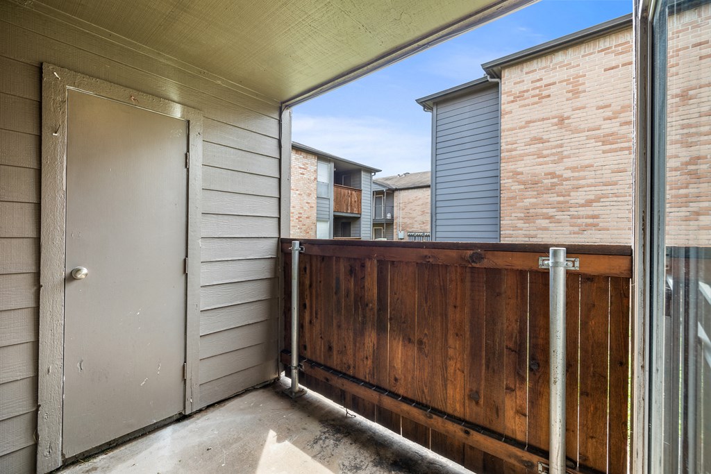 the entrance to a balcony with a wooden fence and a door to a brick building