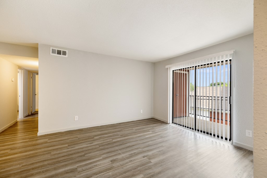 the spacious living room of an apartment with a balcony and wood flooring