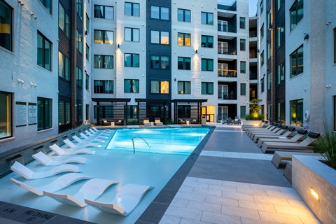 A swimming pool surrounded by lounge chairs in front of a building.