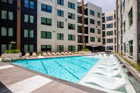 A pool surrounded by buildings and lounge chairs.