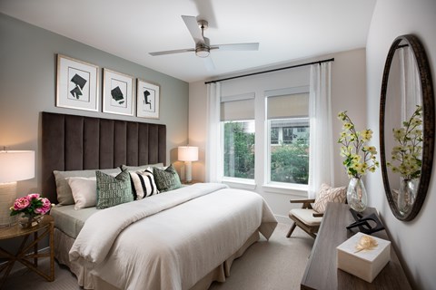 A bedroom with a large bed, a ceiling fan, and a mirror.