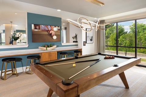 A pool table is in the middle of a room with a bar and a window.