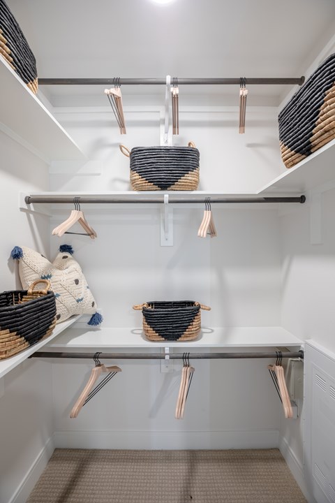 A white closet with clothes hanging on hangers.