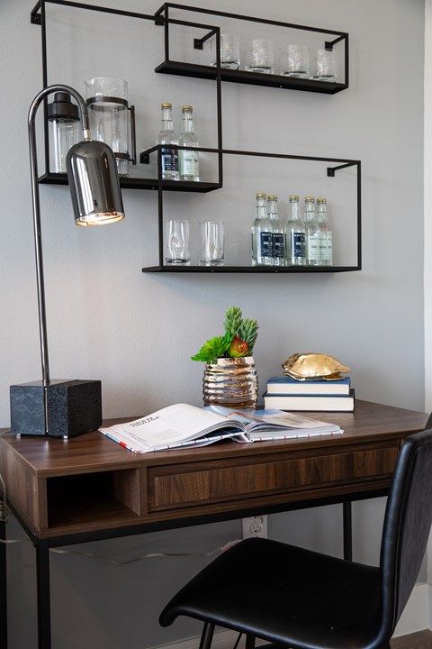 A black chair sits in front of a desk with a lamp and a plant on it.