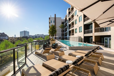 A sunny day at the rooftop pool and lounging area of a modern apartment complex.