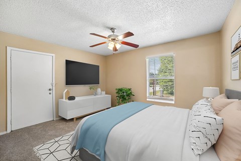 A bedroom with a bed, a television, a window, and a ceiling fan.