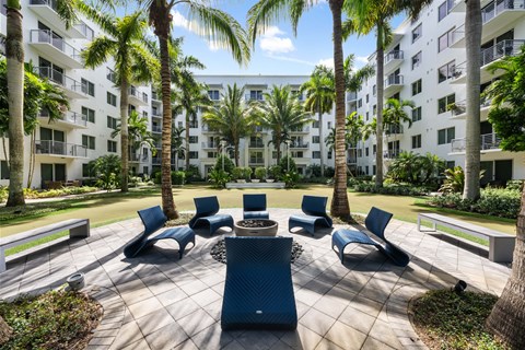 a patio with chairs and palm trees in front of an apartment building