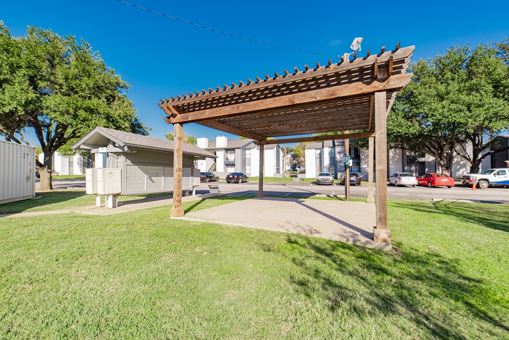 A wooden pergola stands over a grassy area.
