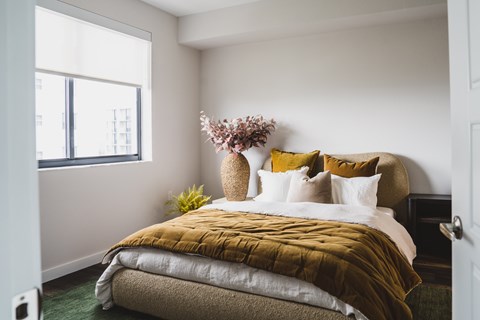 A bedroom with a bed covered in a mustard yellow comforter and a vase of flowers on the bedside table.