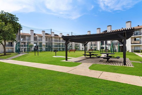 a pergola sits in the middle of a grassy area in front of an apartment