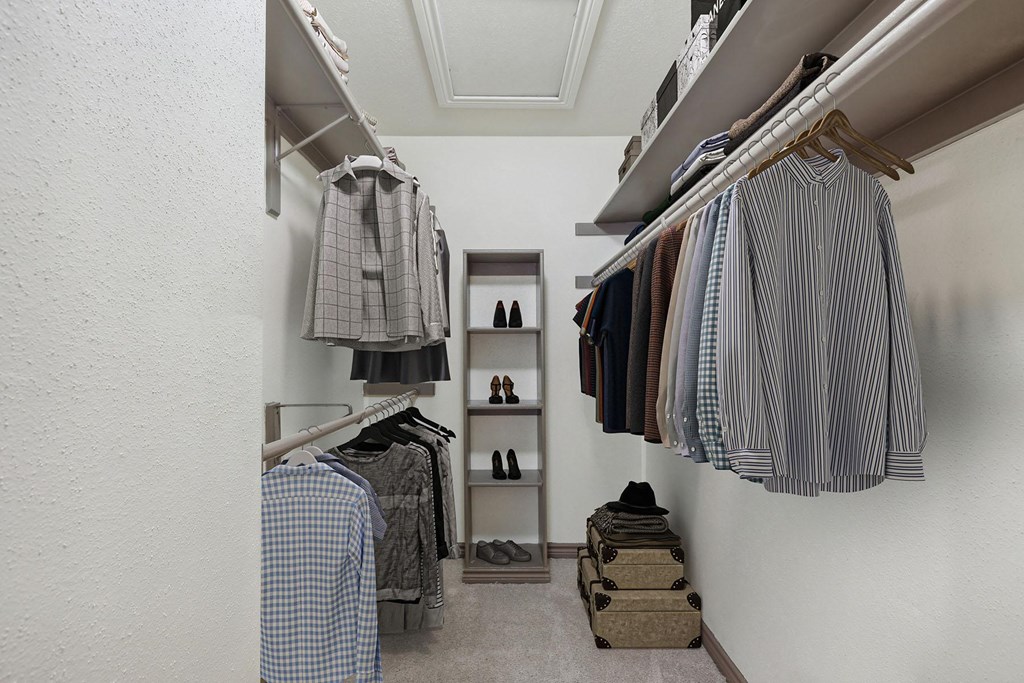 A white closet with clothes hanging and shoes on the floor.