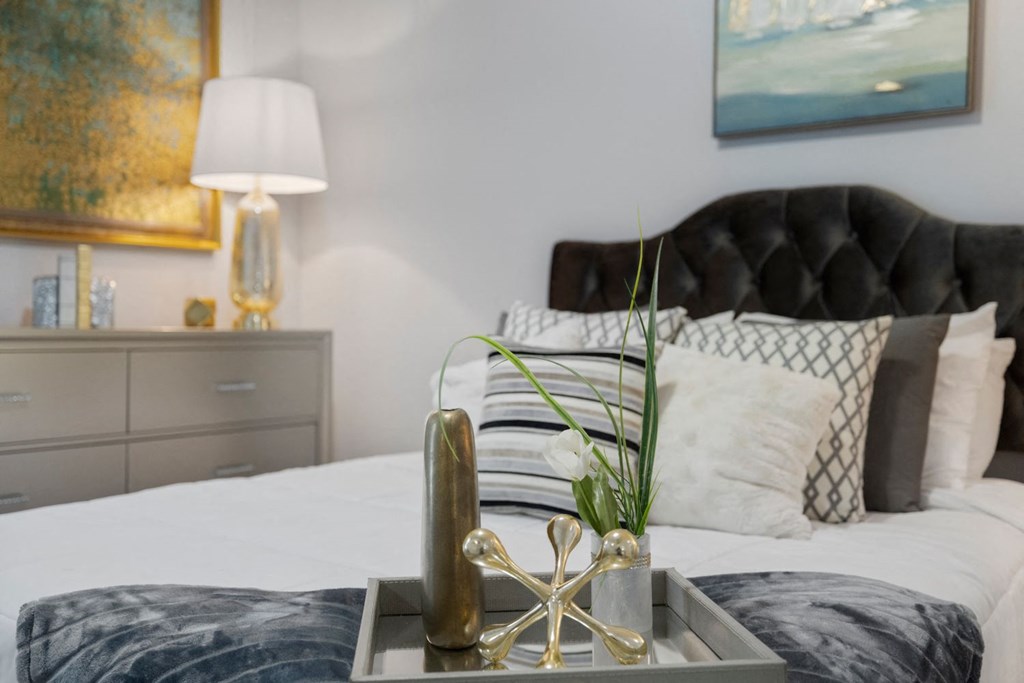 A bedroom with a black headboard and a tray with a plant and a vase on it.
