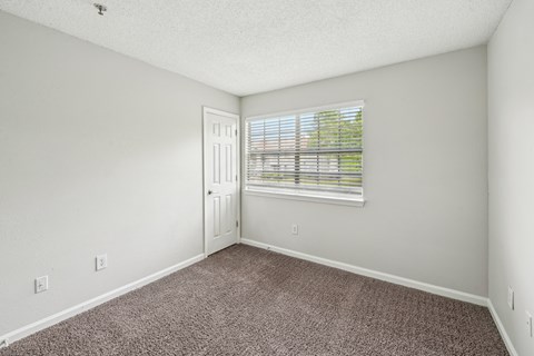 A room with a carpeted floor and a window with blinds.