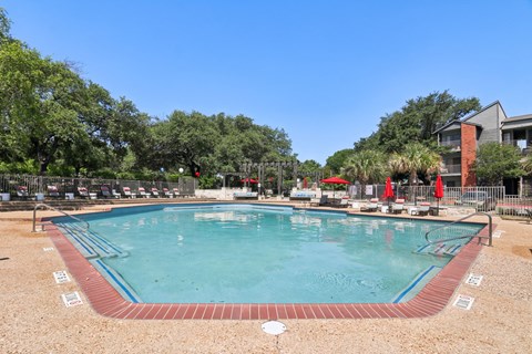 A large outdoor swimming pool surrounded by trees and a fence.