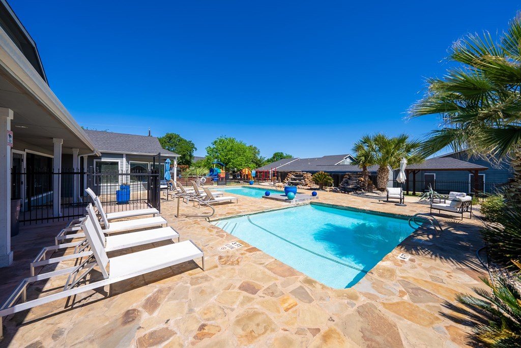 A pool surrounded by a stone patio and lounge chairs.