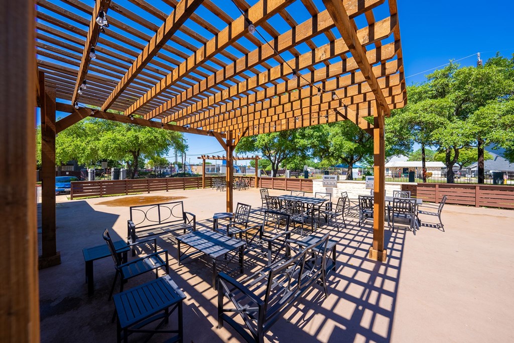 A wooden pergola provides shade for a patio with tables and chairs.