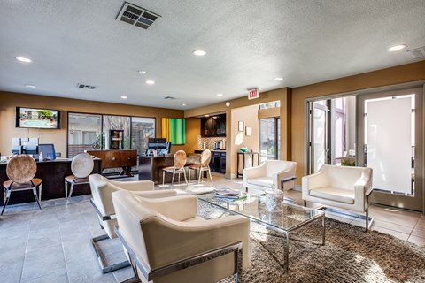 A spacious living room with a glass coffee table and a flat screen TV mounted on the wall.