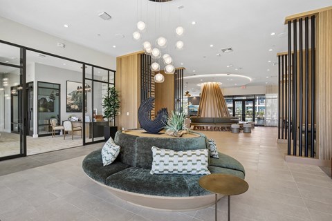 A modern living room with a green velvet sofa and a wooden sculpture on a pedestal.