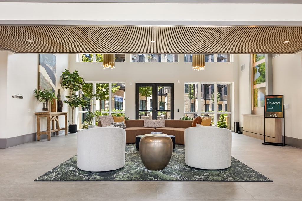 A lobby with a large rug and two white chairs.